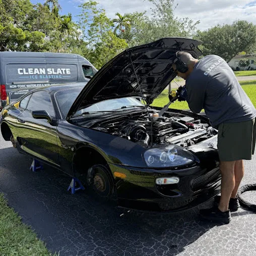 Crew member in a Clean Slate shirt working an engine bay with the branded van parked behind