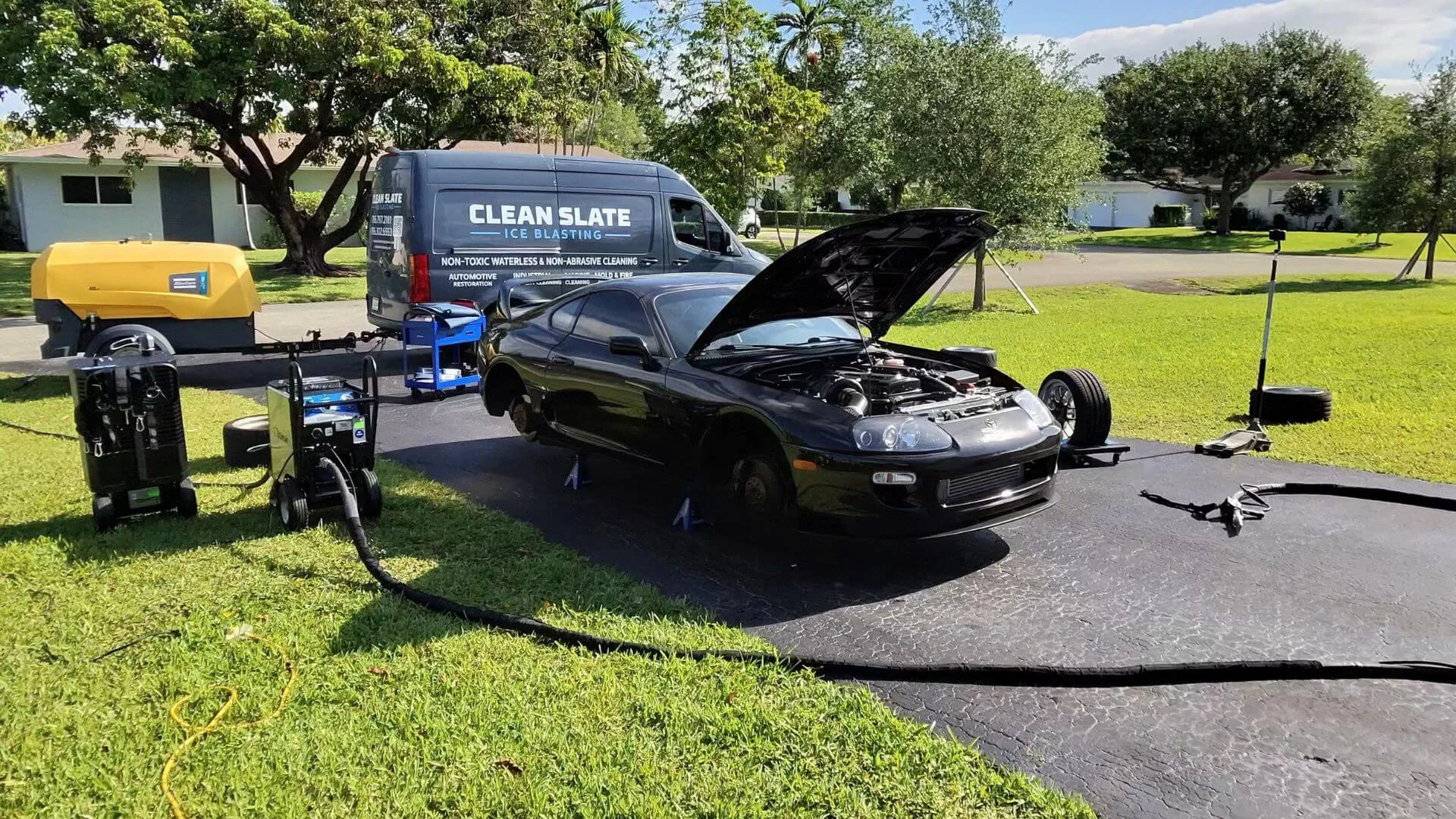 The Clean Slate van, compressor and hose reel set up on a driveway beside a black Supra with the hood raised