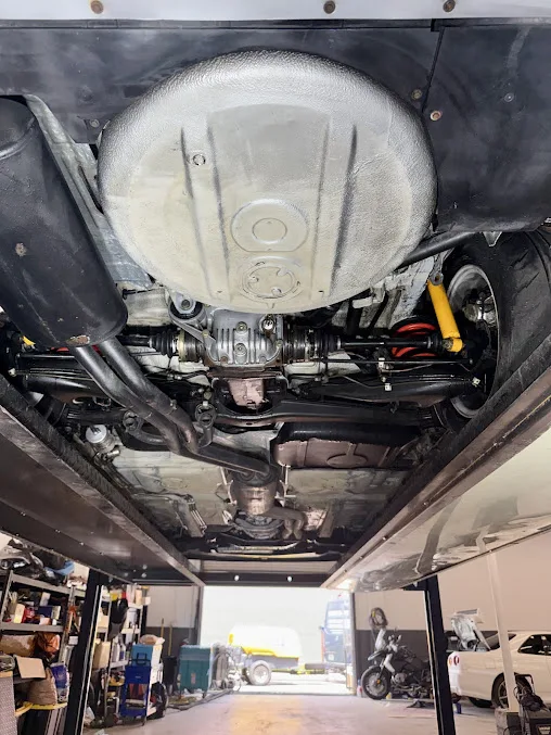 The underside of a car on a two-post lift, fuel tank, driveshaft and differential exposed